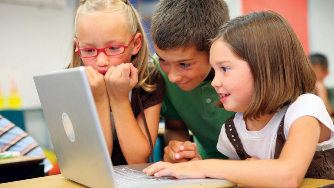 Drei Schulkinder, die vor einem Laptop sitzen