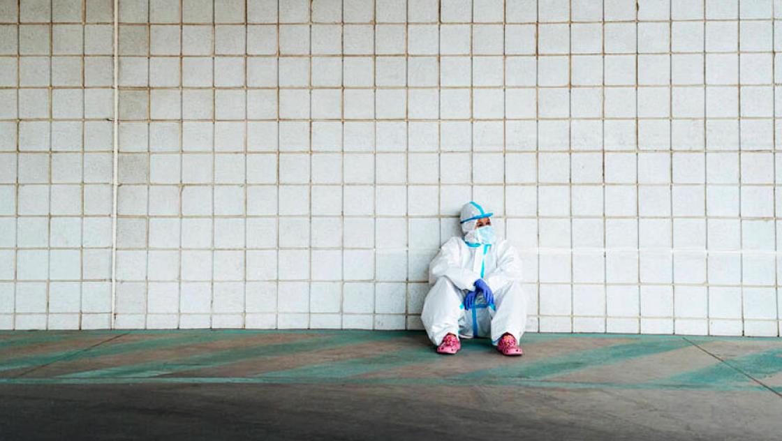 Krankenschwester im Schutzanzug sitzt an einer gefliesten Wand