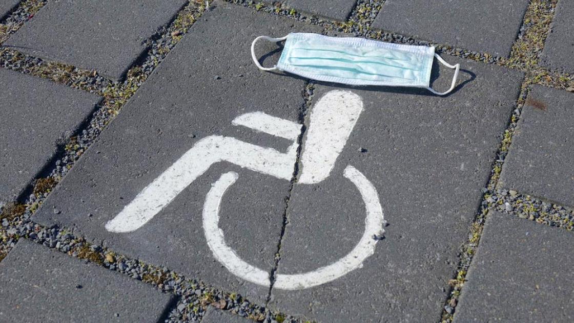 IMAGO / Steinach Auf dem Symbol eines Behindertenparkplatzes liegt ein Mundschutz.