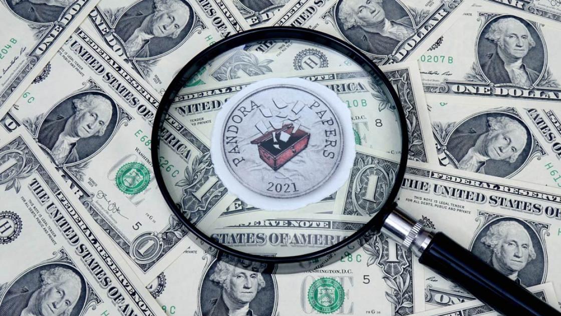 IMAGO / Steinach Auf Dollarscheinen liegt das Logo von Pandora Papers und eine Lupe (IMAGO / Steinach)