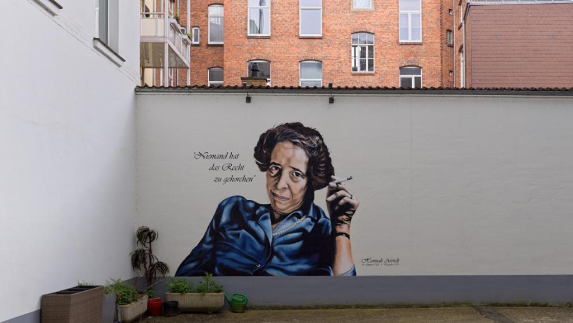 Porträt von Hannah Arendt im Innenhof ihres Geburtshauses. Hannes Grobe (2024) via Wikimedia. Bild zugeschnitten. CC-BY-SA-4.0|https://commons.wikimedia.org/wiki/File:Hannah-arendt3_hg.jpg|
