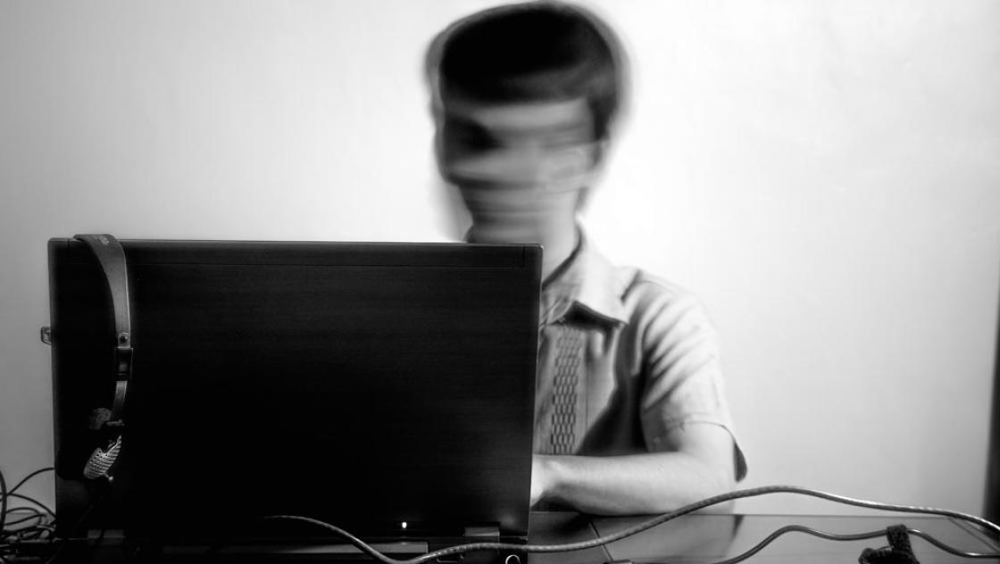 Eine Person mit verschwommenem Gesicht sitzt am Laptop (Road Ahead via unsplash.com)