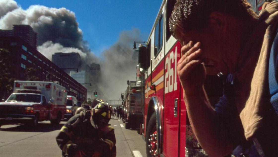 Feuerwehrleute in New York am 11.9.2002. Im Hintergrund sieht man dichte Rauchwolken (IMAGO / United Archives International)