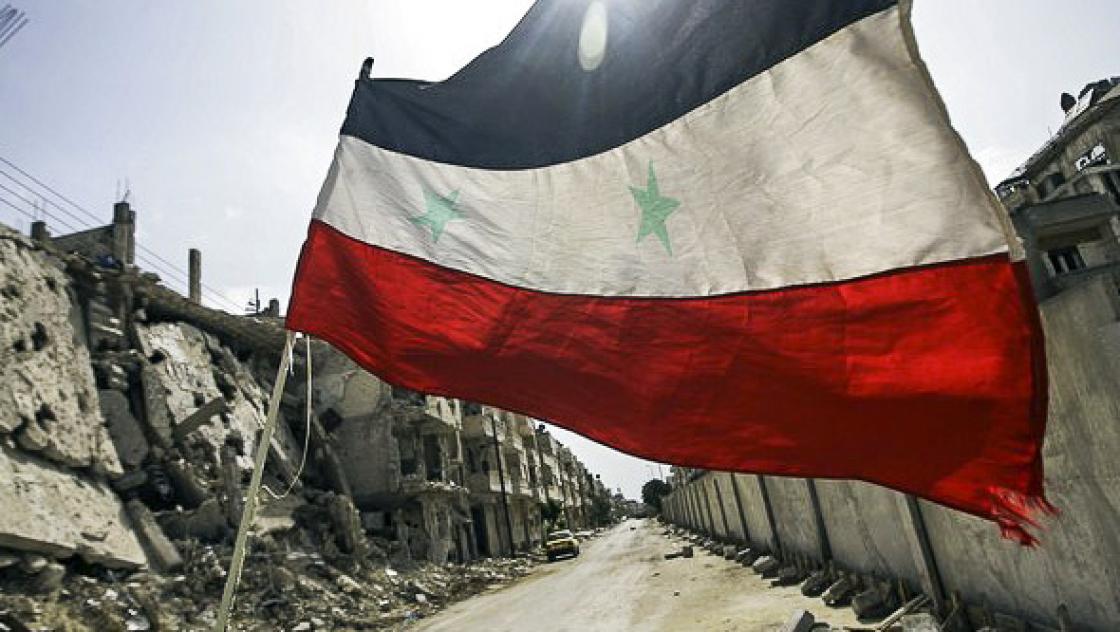 Die syrische Flagge weht über einem vom Krieg zerstörten Straßenzug.
