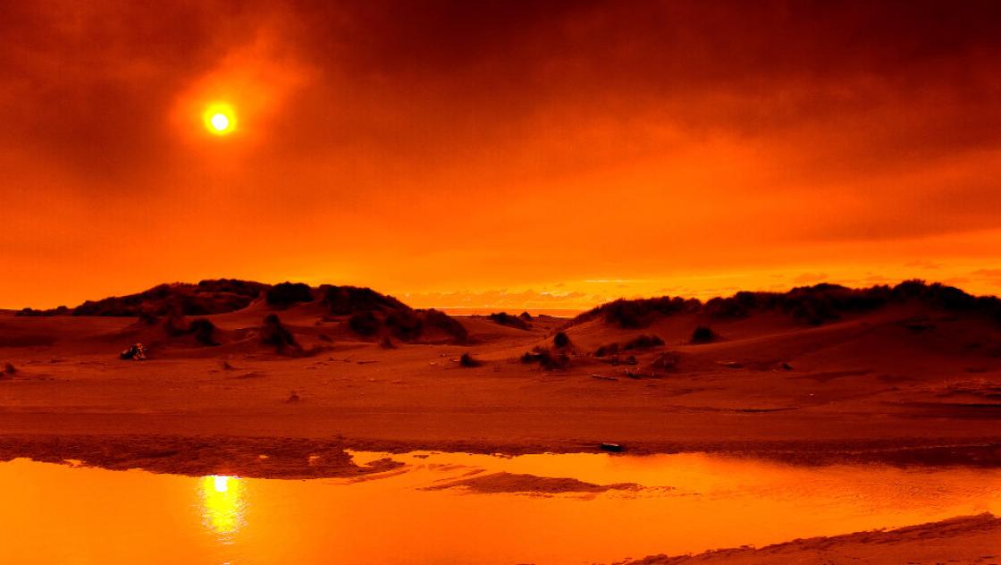 Die Sonne steht über einer in rot getauchten Wüstenlandschaft