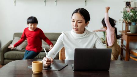 Mutter im Homeoffice mit zwei spielenden Kindern im Hintergrund