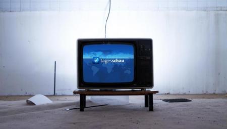 Ein Fernseher mit dem Bild der Tagesschau in einem kahlen Raum