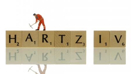 Bauarbeiterfigur auf dem Schriftzug »Hartz IV« (IMAGO / imagebroker)