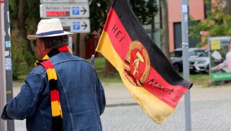 Ein Mann mit DDR-Fahne und Deutschland-Schal. Auf der Fahne ist das Wort »Heimat« zu lesen, 1.7.2023 (IMAGO / BildFunkMV)