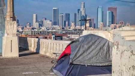 Eine lähmende Bürokratie führt laut Ezra Klein und Derek Thompson im reichen Kalifornien zu einem unnötigen Wohnungsmangel. Zu sehen ist ein Zelt vor der Skyline von Los Angeles, 27.1.2024 (IMAGO / Newscom World / Peter Bennett)