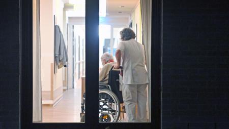 Pflegekraft schiebt eine Person im Rollstuhl in einem Flur in einem Altenheim im Landkreis München, 14.1.2025 (IMAGO / Sven Simon)