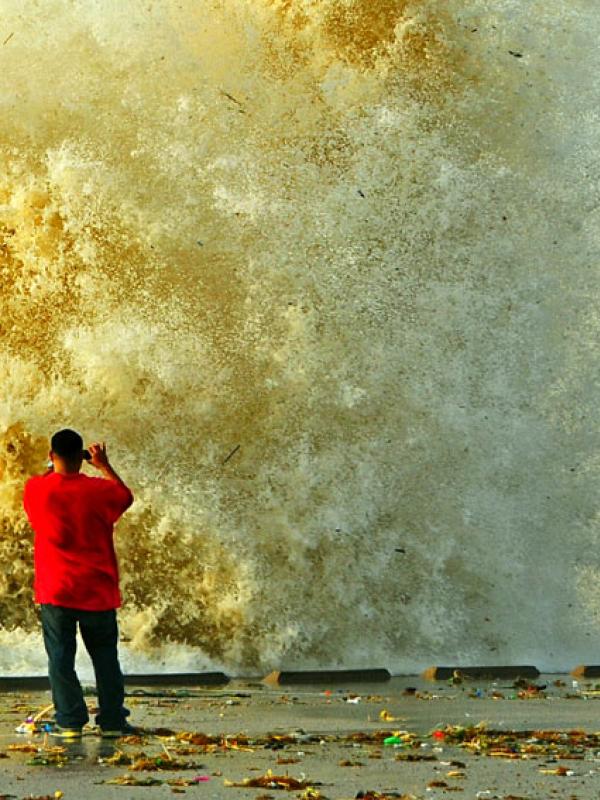 Ein Mann fotografiert eine Welle, die sich an einer Kaimauer bricht
