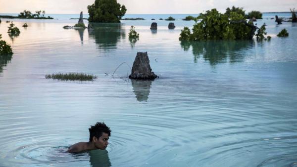 Der 16jährige Peia Kararaua schwimmt durch ein überschwemmtes Gebiet, um sein Haus im Dorf Aberao im pazifischen Inselstaat Kiribati zu erreichen (IMAGO / ZUMA Press) 