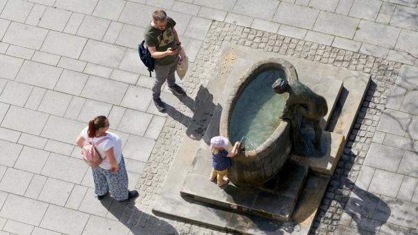 Eine Familie an einem Brunnen im Stadtzentrum von Magdeburg, 25.6.2022 (IMAGO / Panthermedia)