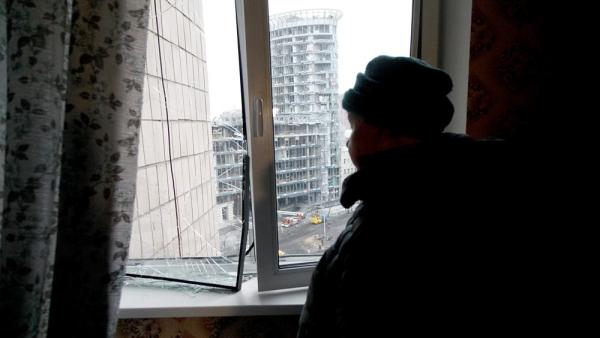 Eine Frau steht an einem Fenster und blickt auf ein durch einen russischen Raketenangriff beschädigtes Gebäude, Kiew, Ukraine, 18.1.2025 (Kirill Chubotin / IMAGO / NurPhoto)