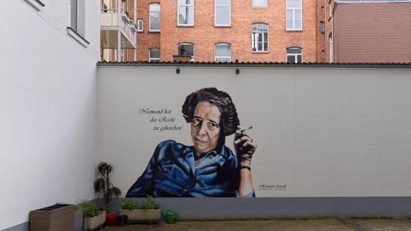 Porträt von Hannah Arendt im Innenhof ihres Geburtshauses. Hannes Grobe (2024) via Wikimedia. Bild zugeschnitten. CC-BY-SA-4.0|https://commons.wikimedia.org/wiki/File:Hannah-arendt3_hg.jpg|